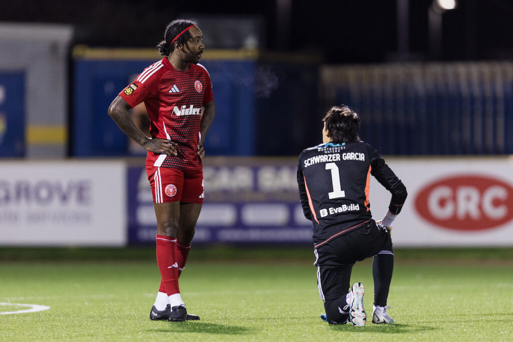 Newtown's Desean Martin and Newtown's goalkeeper Garcia Schwarzer during the 2024/25 JD Cymru Premier Play-Off Conference league fixture between Barry Town United FC and Newtown AFC at Jenner Park Stadium, Barry, Wales