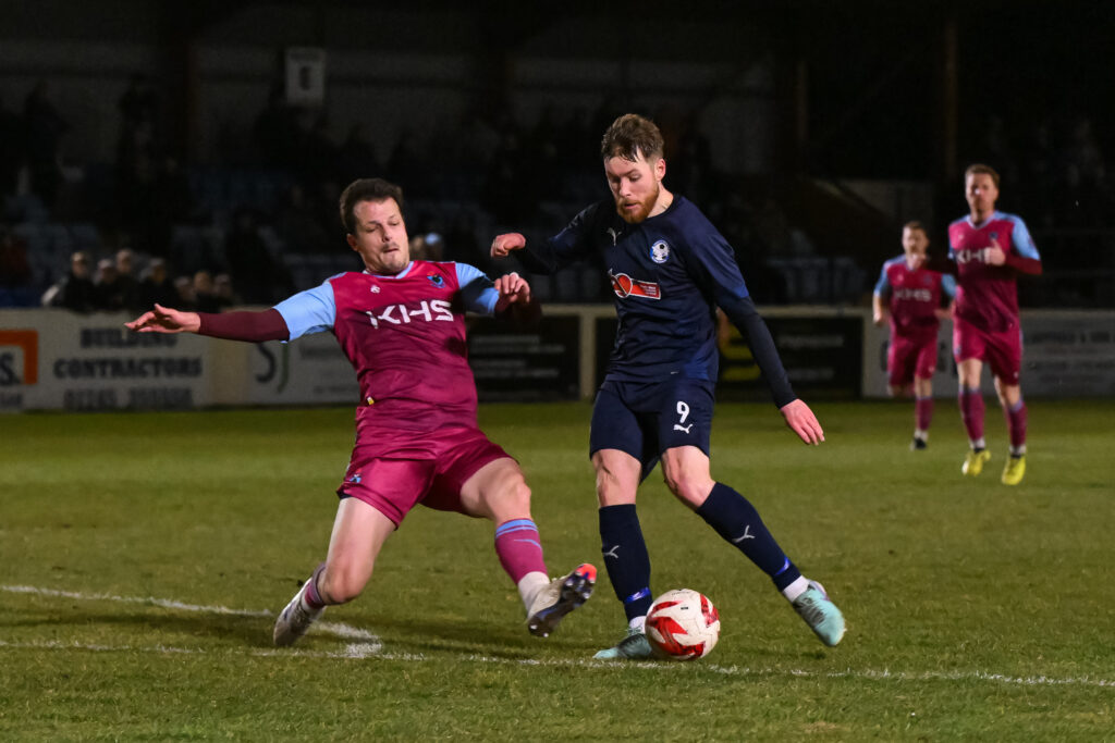 Jordan Evans of Airbus UK Broughton shoots on goal but is tackled by Lewis Sirrell of Colwyn Bay during the Welsh Blood Service League
